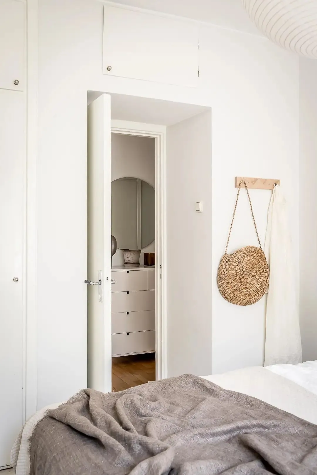 A cozy, minimalist bedroom featuring a woven basket, wooden furniture, and textured bedding.