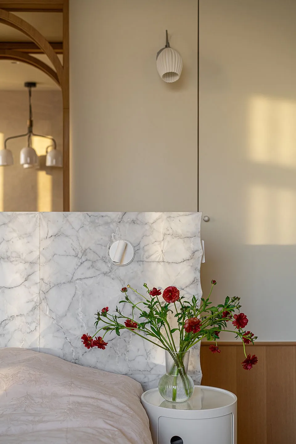 A minimalist bedroom featuring a marble headboard with red flowers in a vase on a bedside table.
