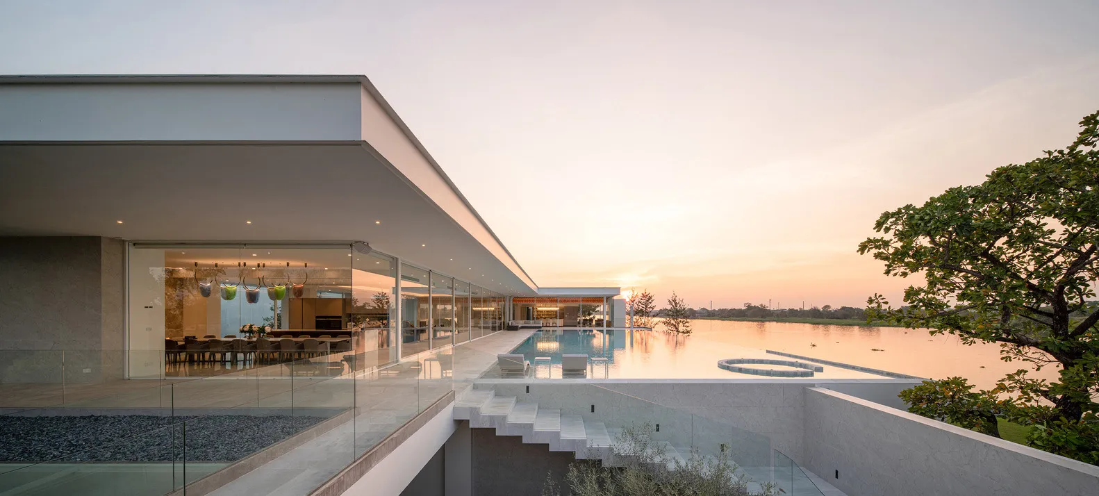 A modern residential building with glass walls and a rooftop pool overlooking a serene lake.