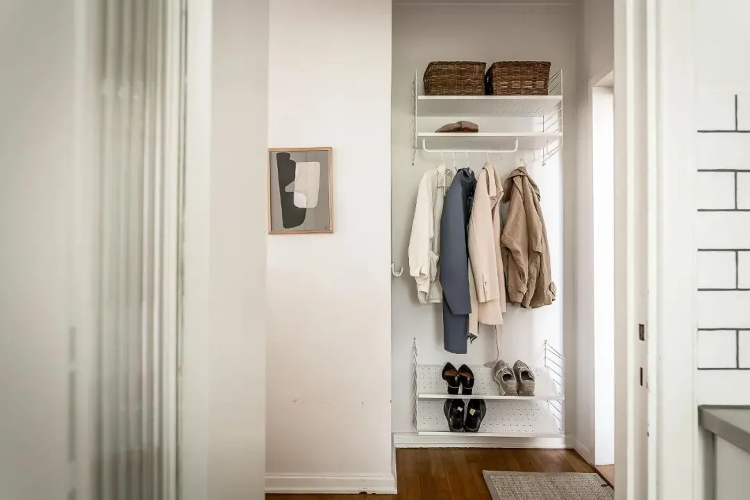 Modern white metal shelving system with woven storage baskets in a minimalist closet.