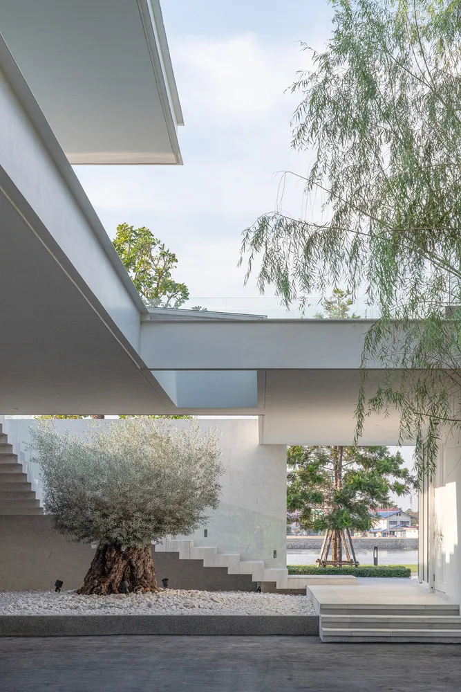 An indoor staircase with a concrete base surrounded by a gravel patio, leading to a green area with trees and a light blue sk
