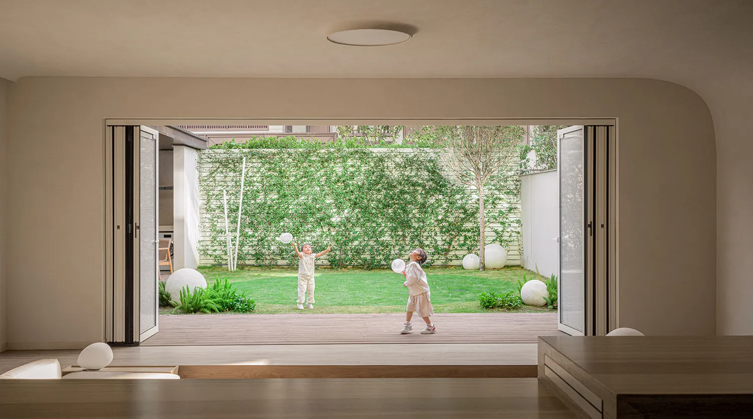 Two children playing badminton outdoors in a modern residential playarea with wooden deck and greenery.