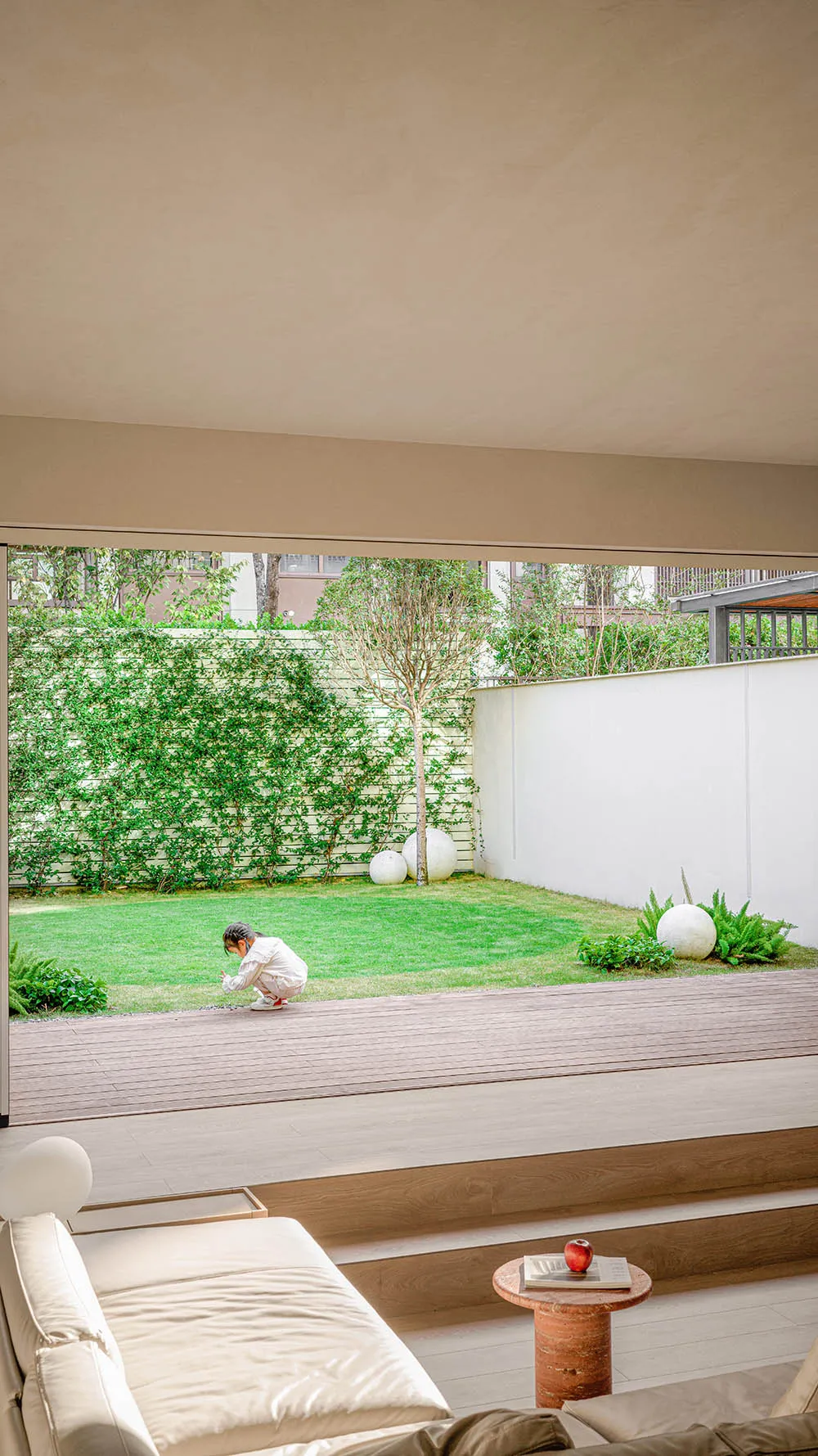 A modern minimalist living room with a white couch, wooden flooring, concrete walls, and lush greenery.