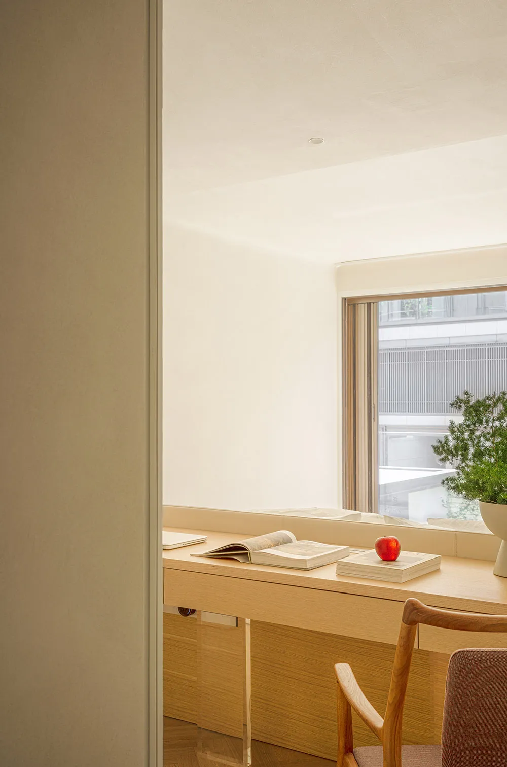 A minimalist home office setup featuring a wooden desk with books and an apple.