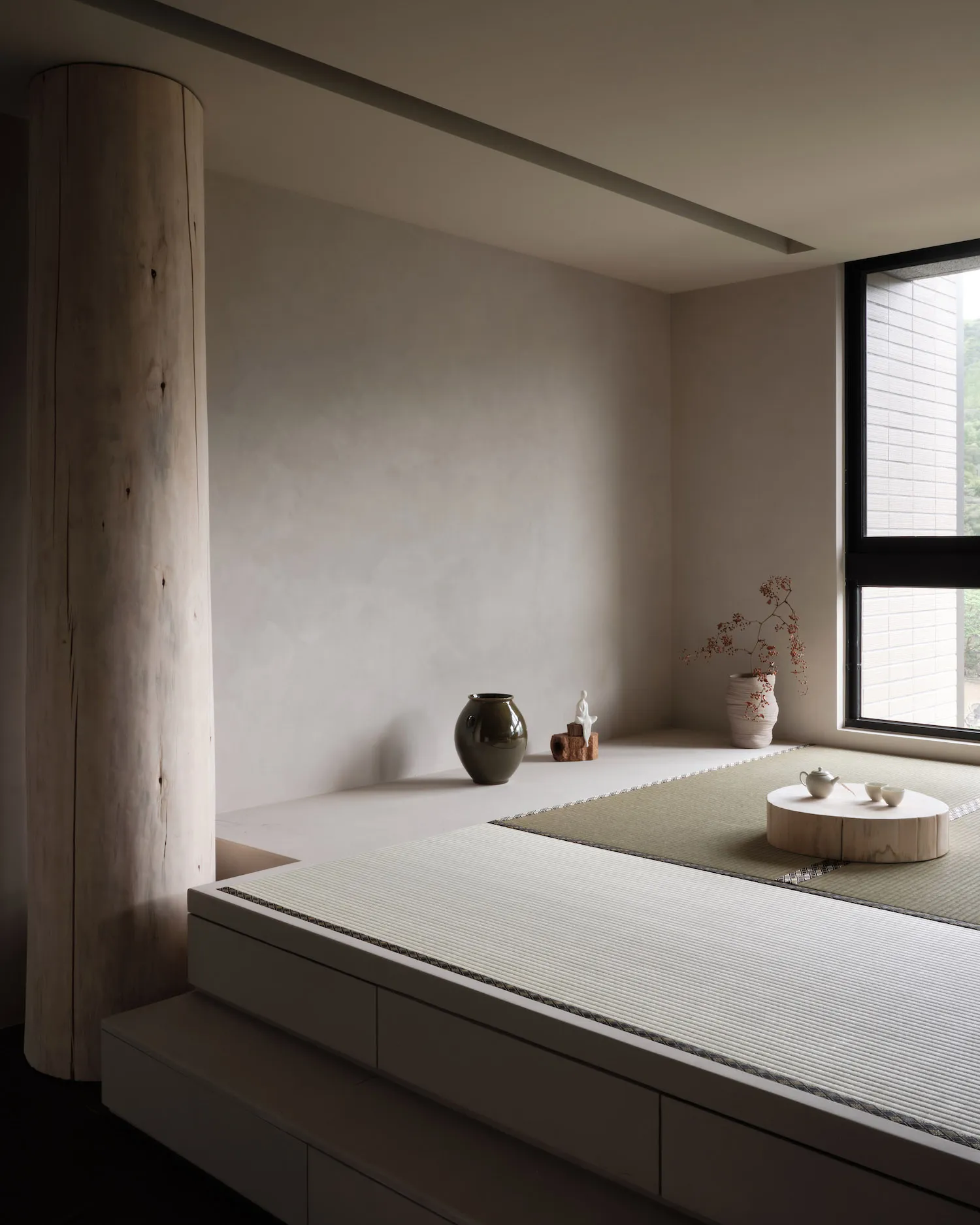A minimalist living room featuring wooden furniture, a tatami mat, and a small tea set on a wooden platform.