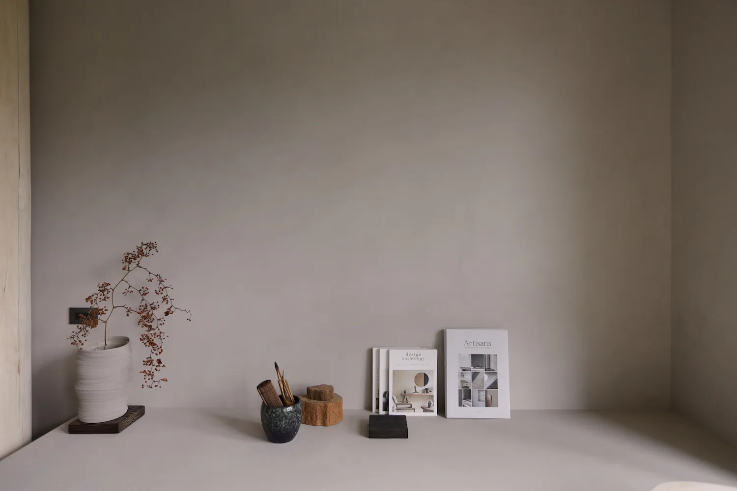 A minimalist shelf with ceramic vases, books, and a potted plant.