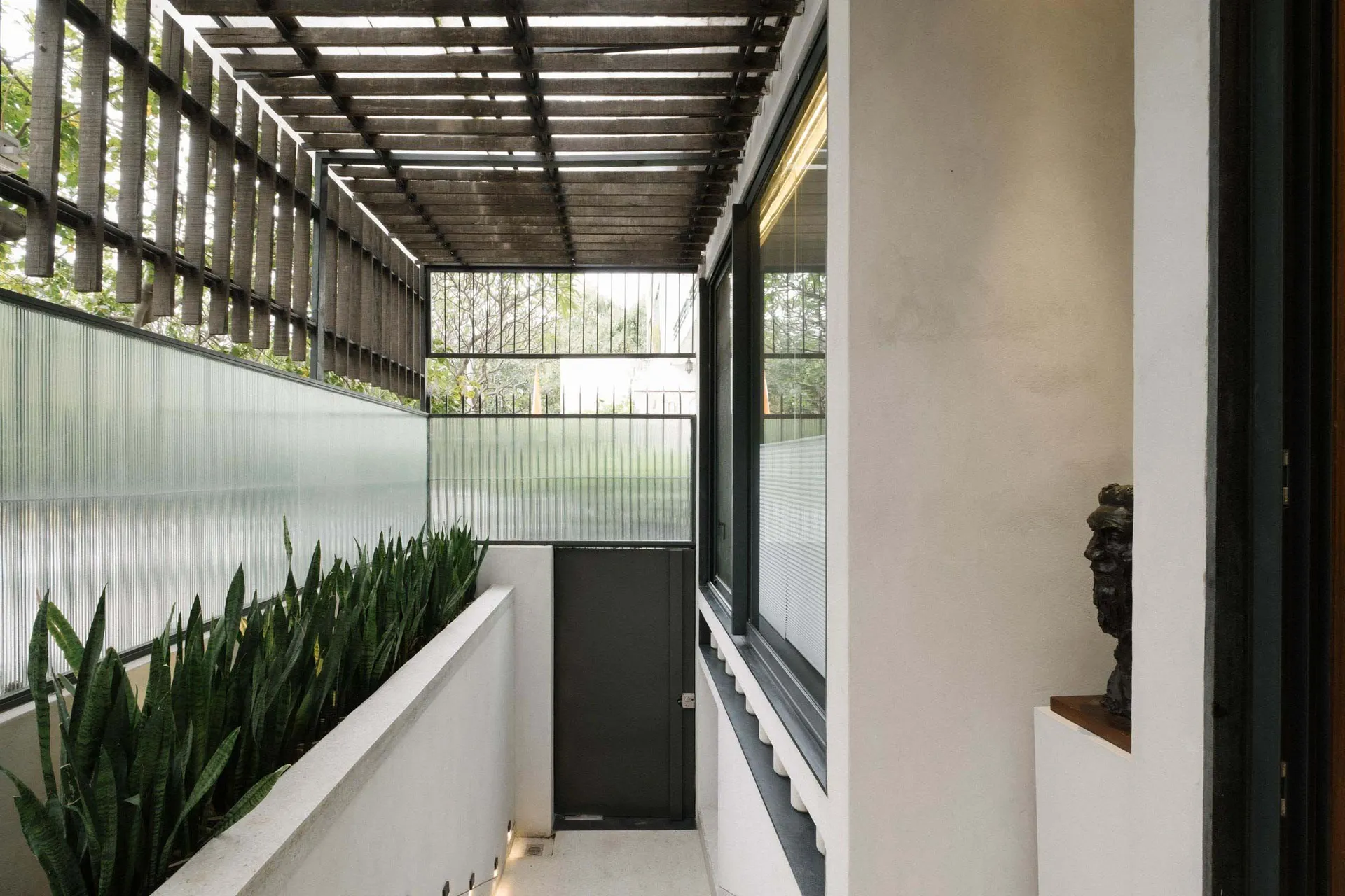 Glass facade with a wooden pergola and plants on a modern building exterior.