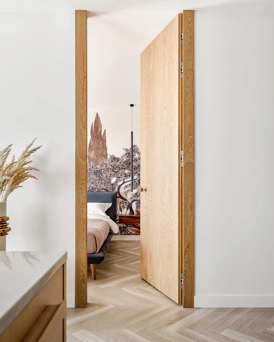 Modern minimalist bedroom featuring a wooden door and herringbone wood flooring.