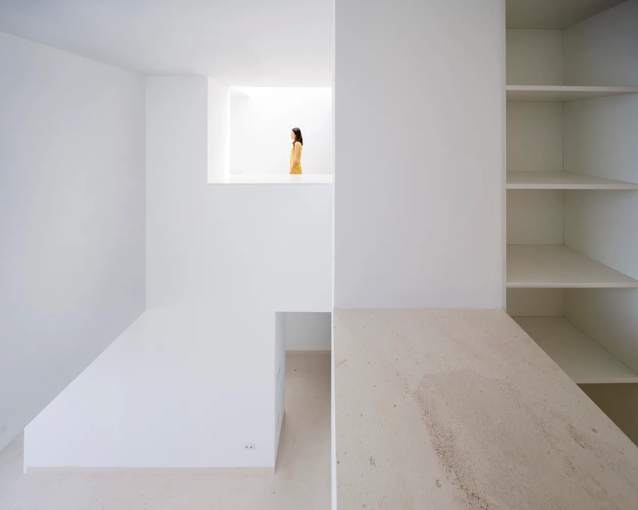 A minimalist interior with concrete walls and floor, featuring a solitary figure in a window.