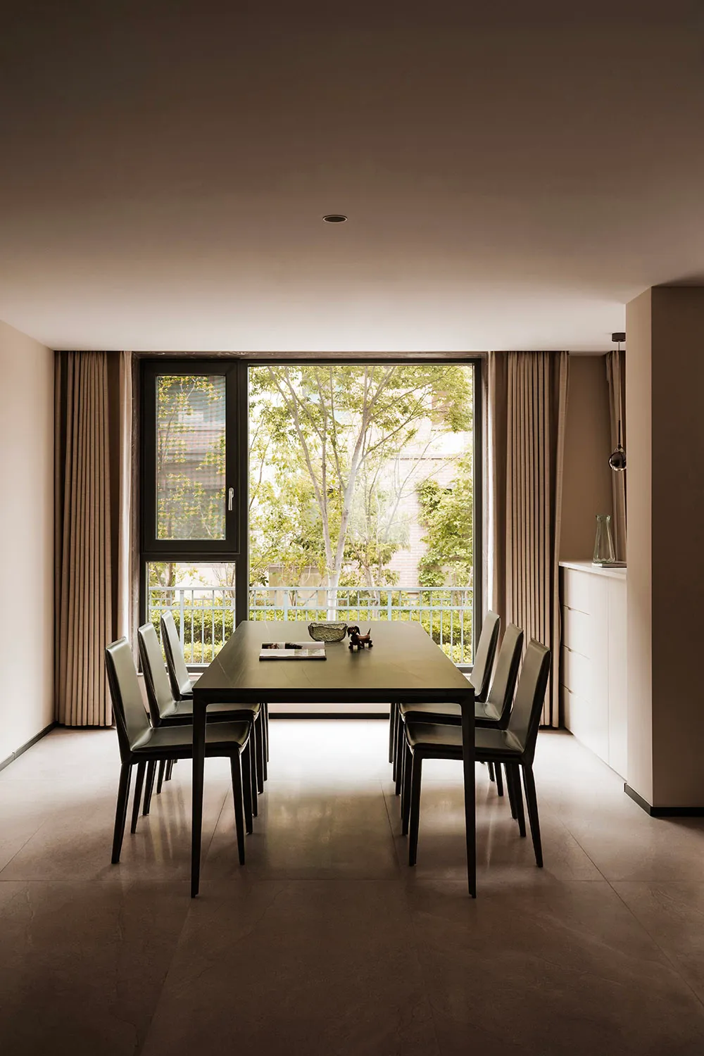 Modern dining room with black leather chairs and black rectangular dining table, large glass window with trees outside, brown