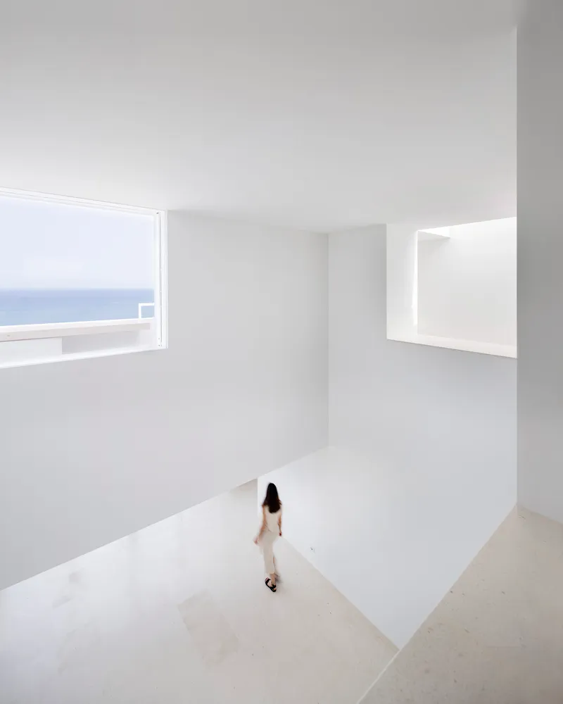 A minimalist white interior space with a large window overlooking the ocean.