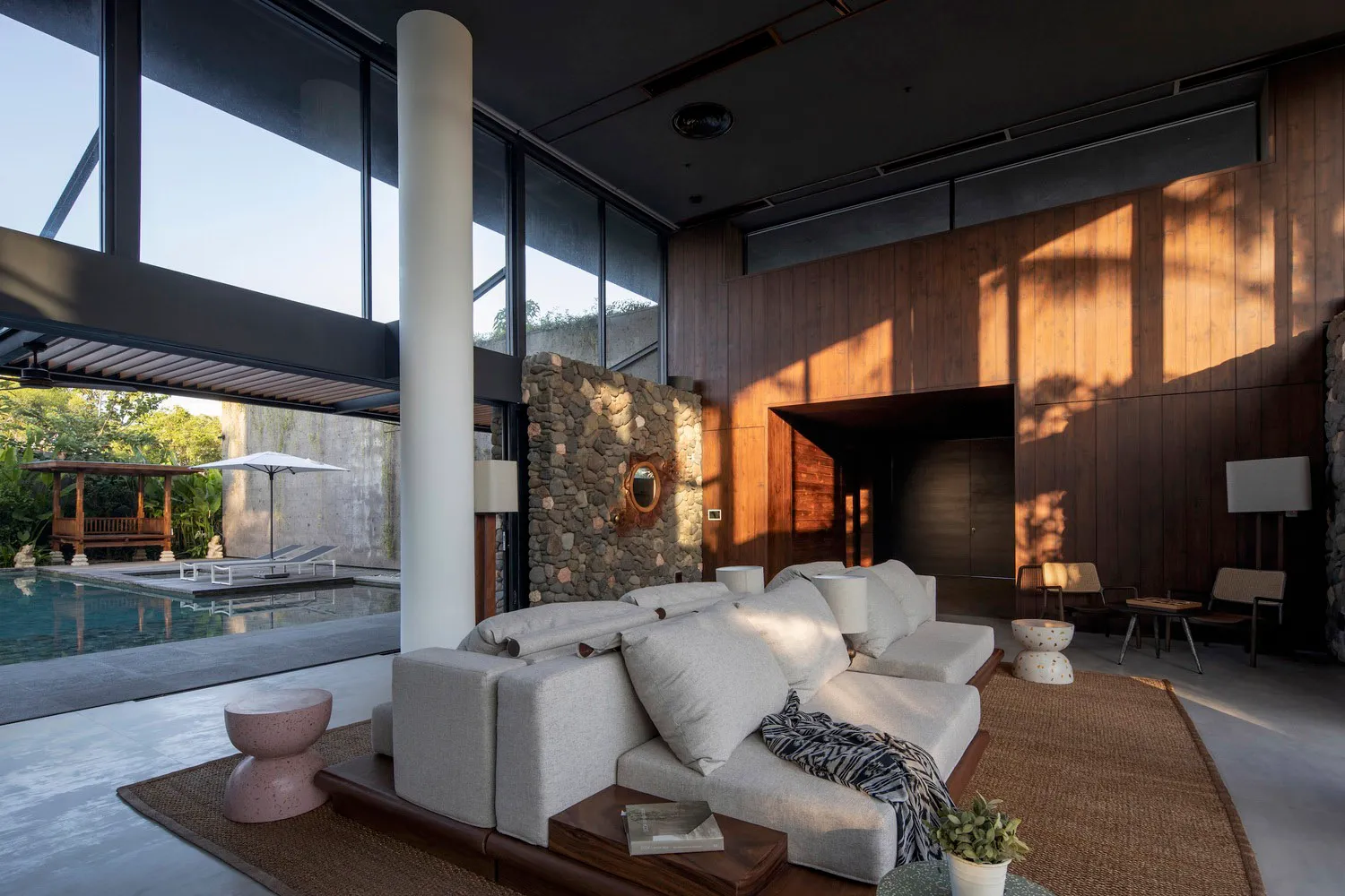 A modern living room with a natural stone accent wall and a large sofa in front of a large windows.