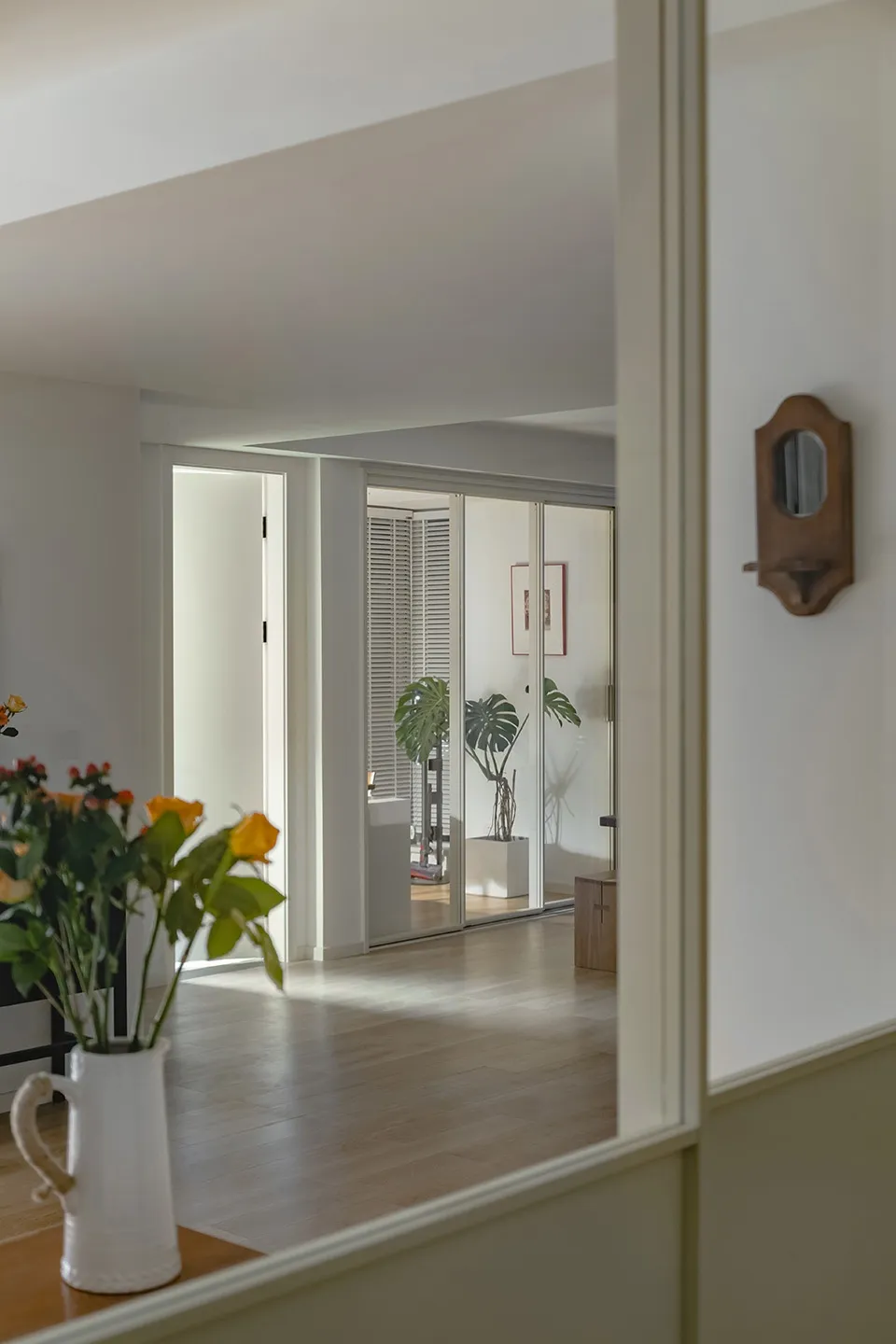 A modern living room with white walls, wooden flooring, and a vase of flowers.