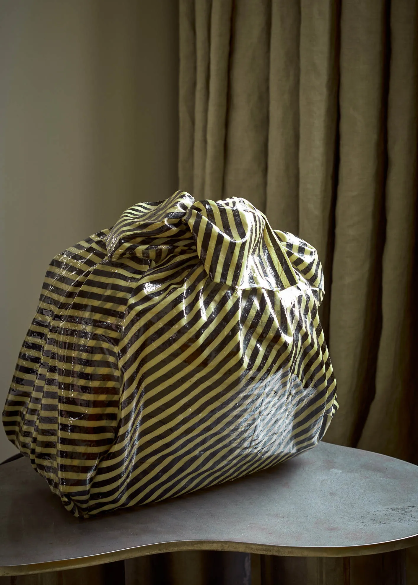 A large, plastic-wrapped trash bag with black and yellow diagonal stripes sits on a round, metallic tabletop.