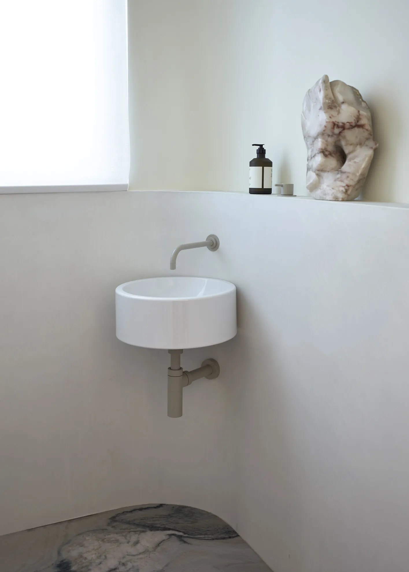 A minimalist modern bathroom with a circular sink, marble sculpture, and bottle of liquid.