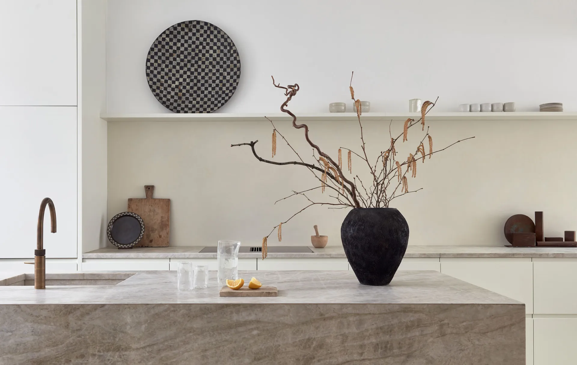Modern minimalist kitchen with marble countertops and a black vase with dried branches.