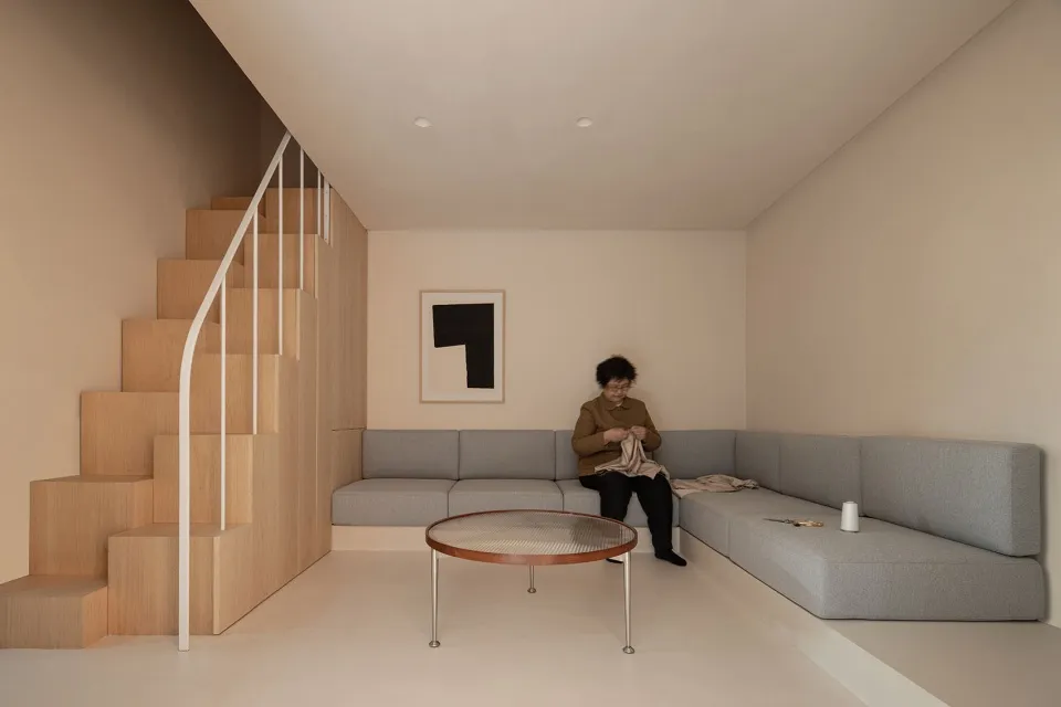 A minimalist living room featuring a grey fabric sofa, a modern coffee table, and a wooden staircase.