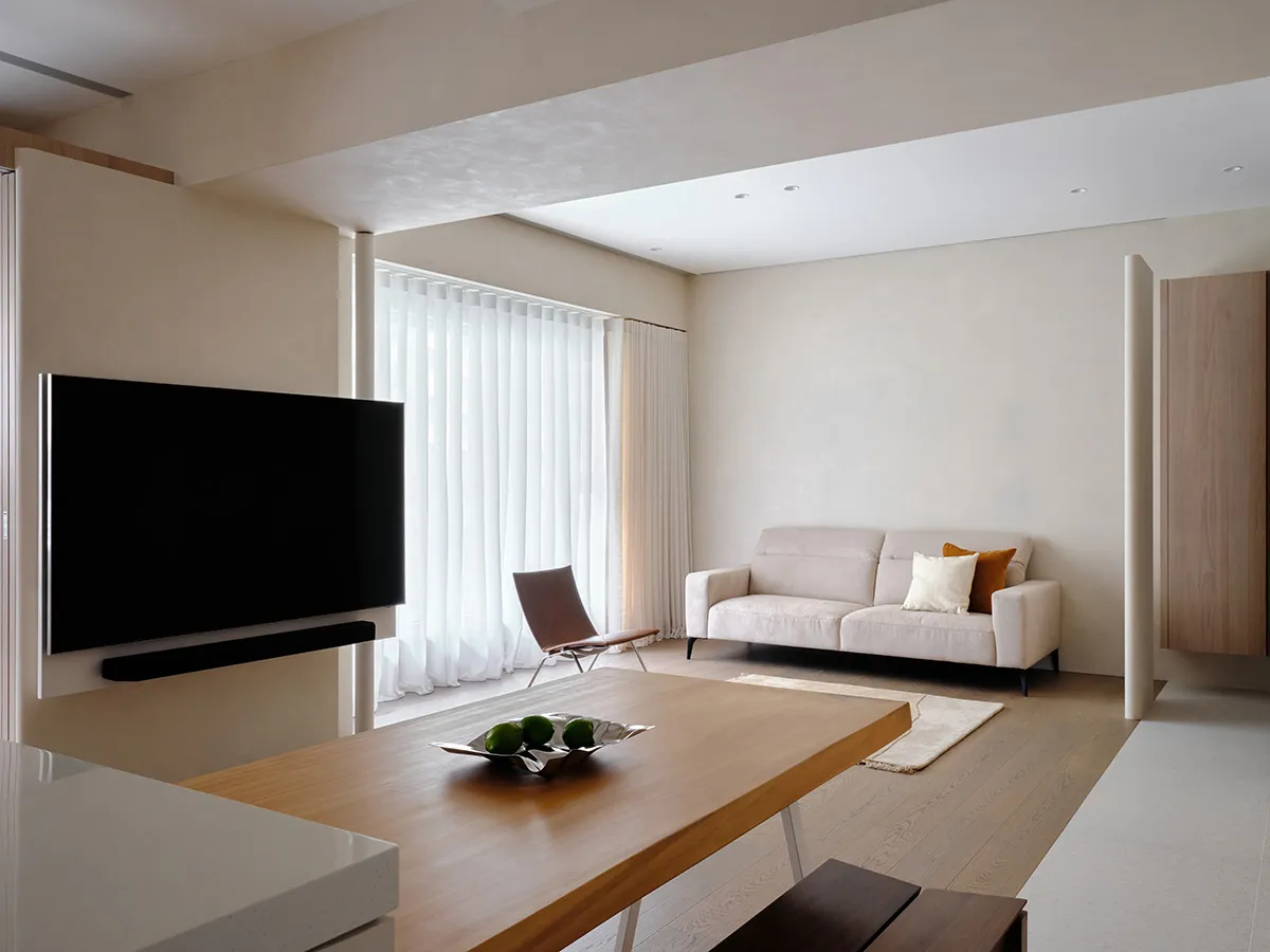 A minimalistic living room with light-colored walls, a white couch, and a wooden table.