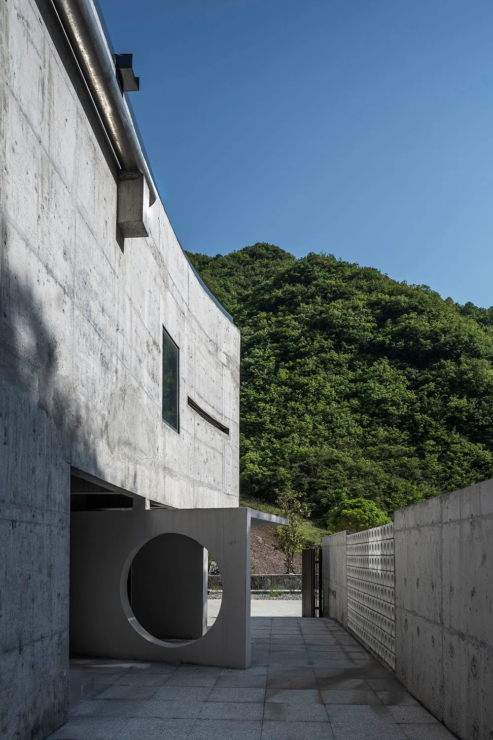 A modern house with a circular doorway and a concrete exterior, featuring a minimalist design and a courtyard surrounded by g