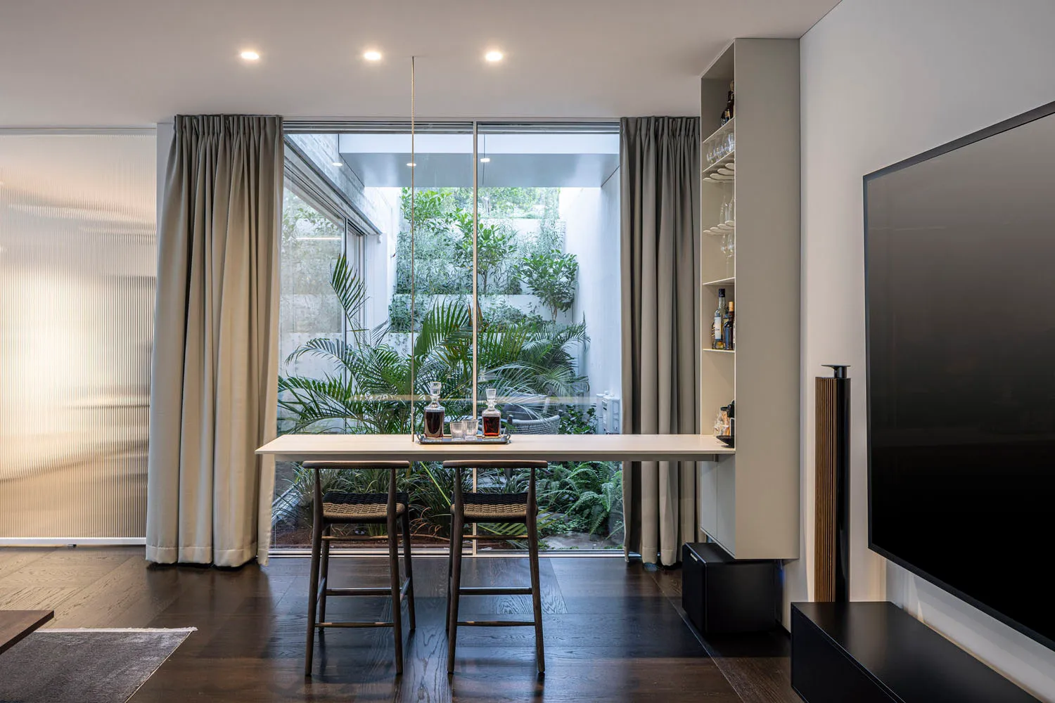 A modern living room featuring a high-end interior design with wooden floors, glass walls, and a mix of materials.