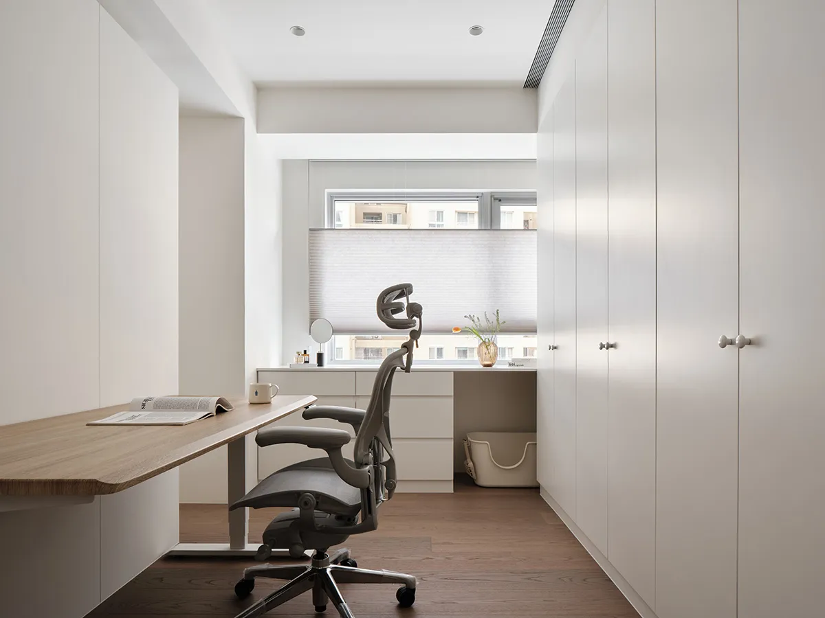 A modern minimalist home office featuring a wooden desk, glass window, and ergonomic chair.