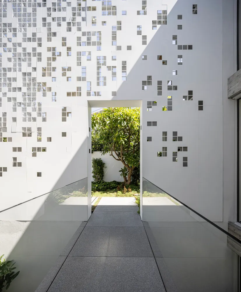 A modern white wall with glass windows and a walkway leading to a garden with greenery and trees.