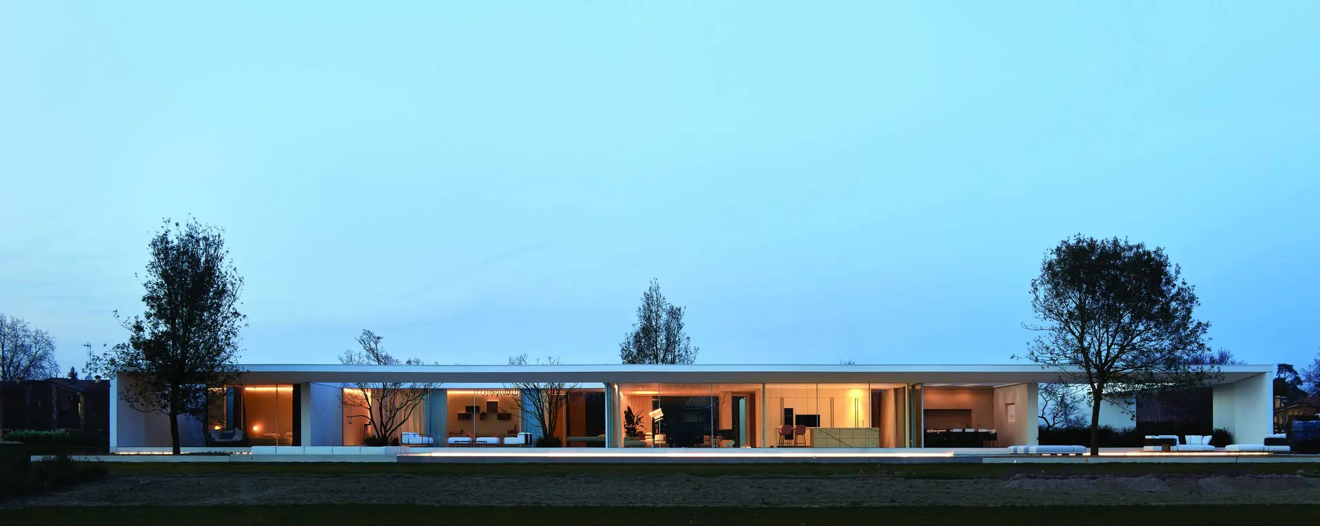 Modern residential exterior with glass and concrete materials, illuminated at dusk.