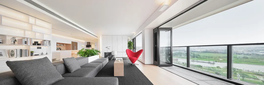 Modern minimalist living room with a grey sofa, red chair, and wooden floor.