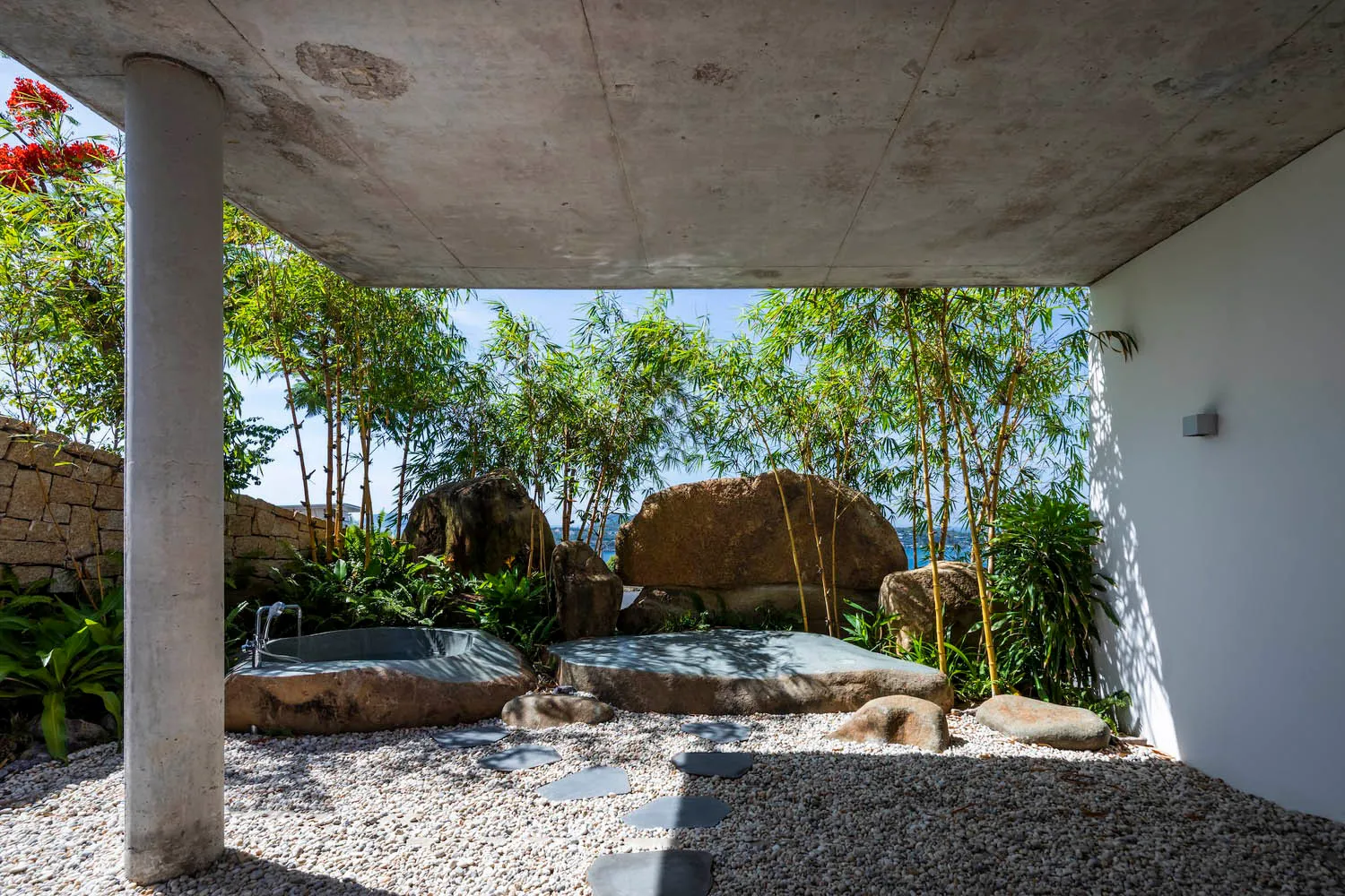 A sleek concrete outdoor bathroom with natural stone features and lush greenery.