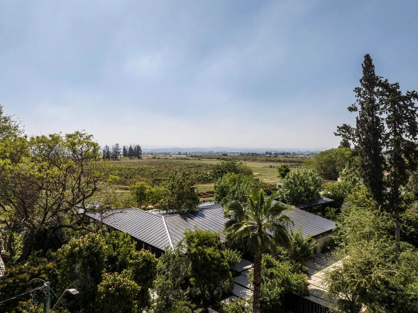 A modern residential property with a metallic roofing system surrounded by lush greenery.