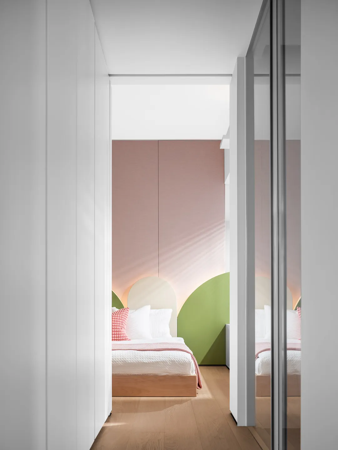 A minimalist bedroom with light-colored walls and white flooring, featuring a single twin bed with wood-textured headboard an
