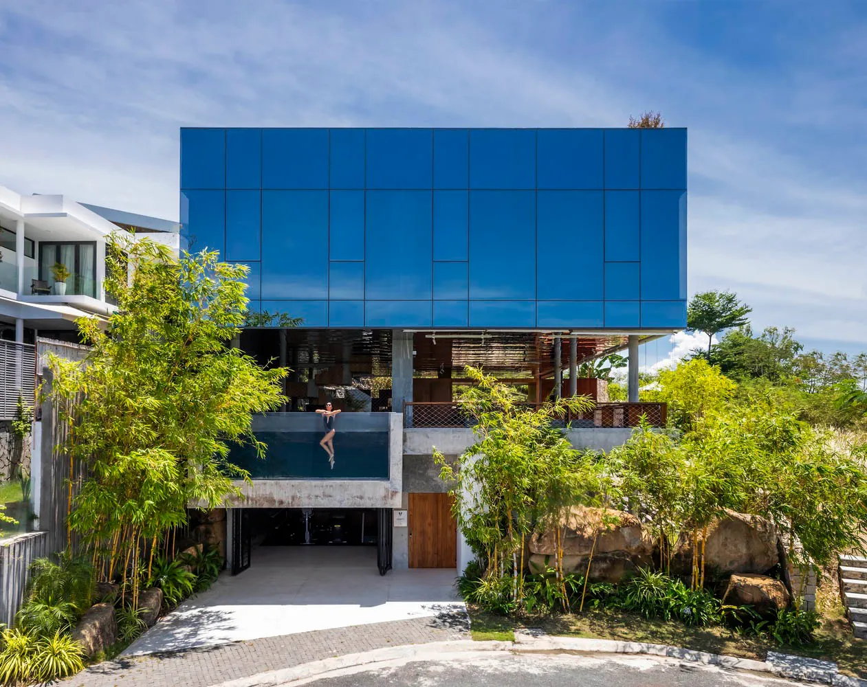 A modern house featuring a glass and concrete exterior with lush greenery surrounding it.