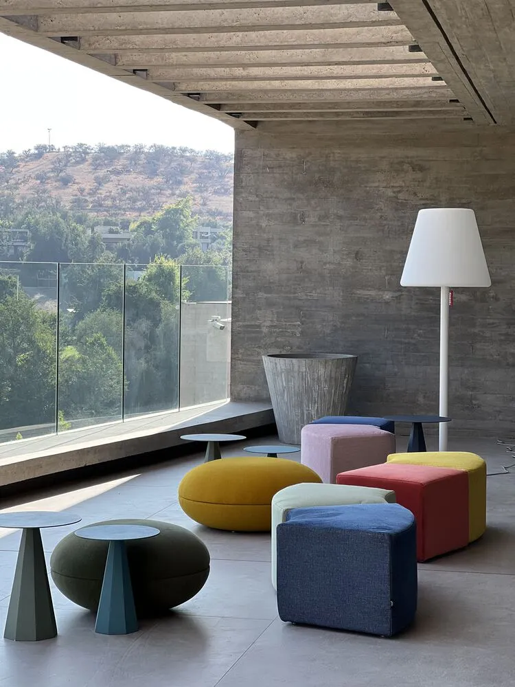 A modern indoor space featuring concrete walls and colorful textile ottomans and tables.