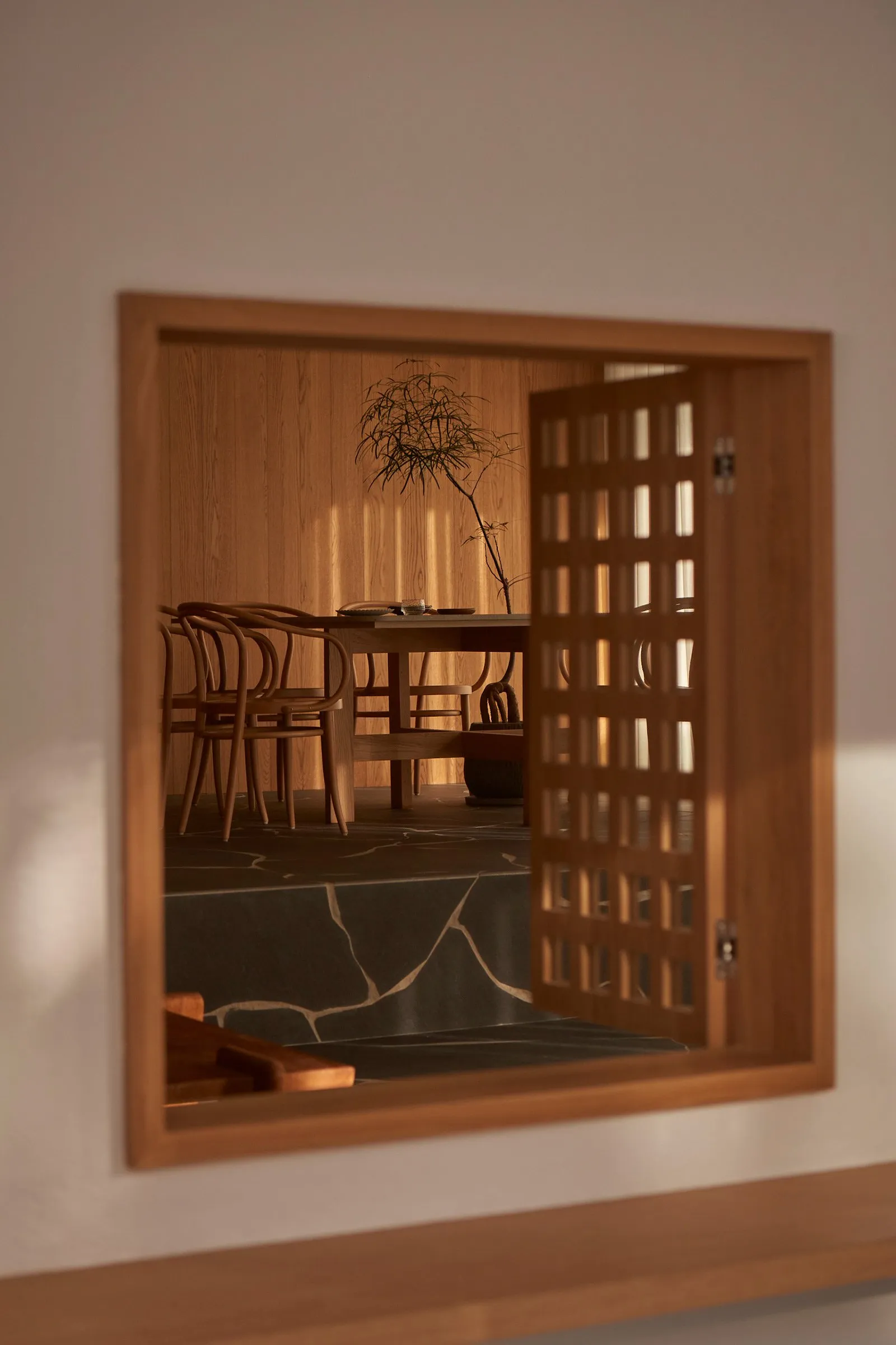 A view of a restaurant interior through a wooden sliding door with a lattice design, featuring a wooden dining table, chairs,