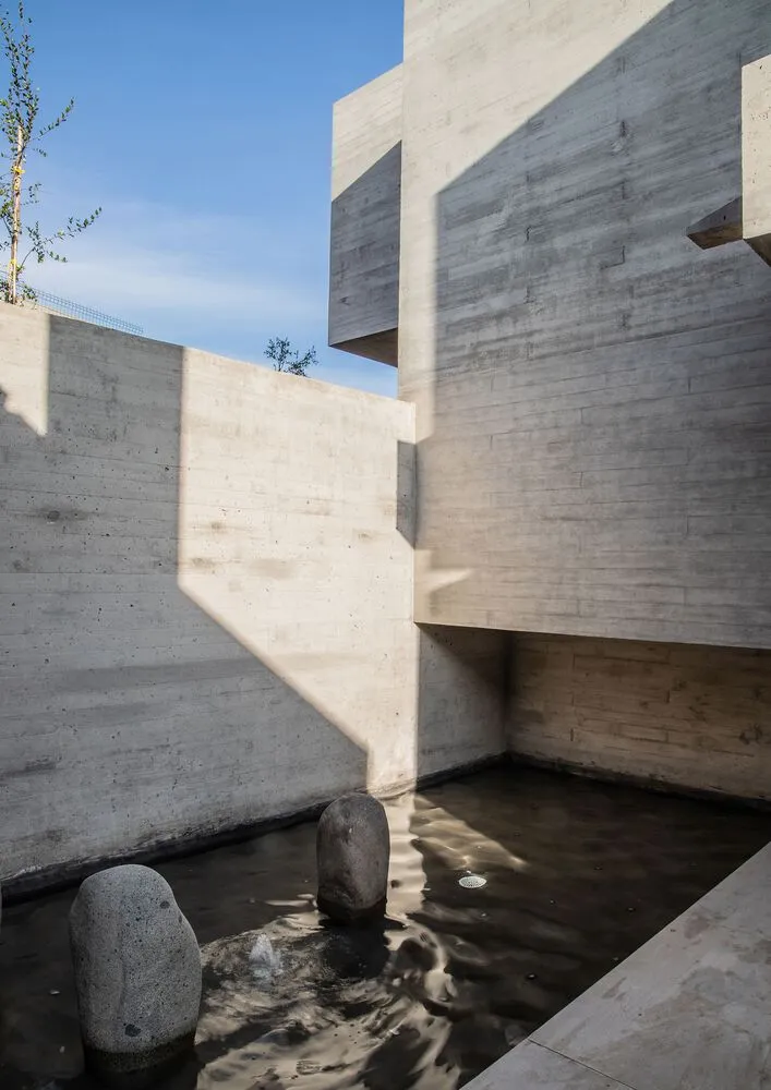 Modern architecture featuring concrete walls and a small pond with rocks.