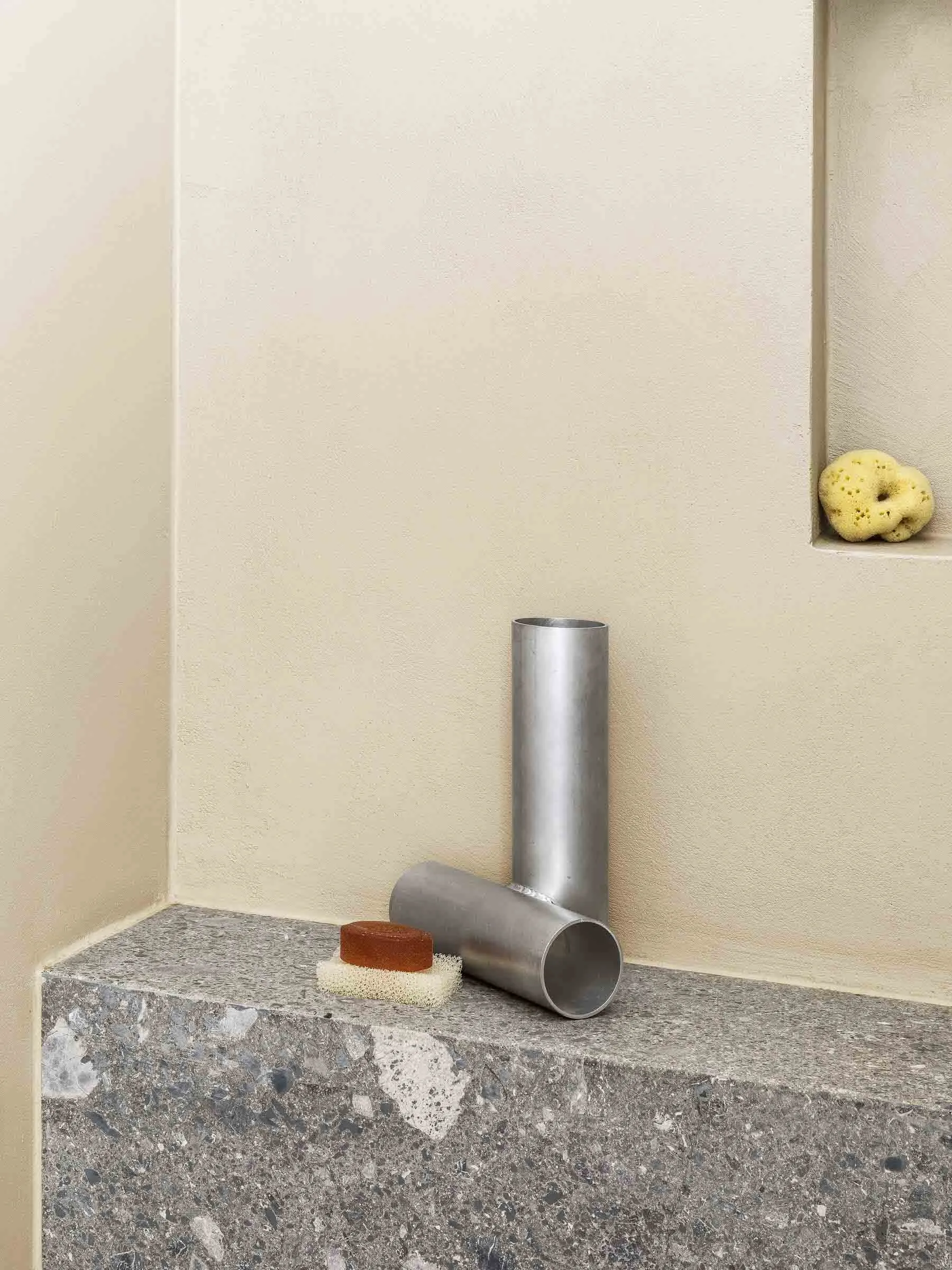 A modern bathroom with a concrete tub, featuring a unique metal caddy holding a bar of soap, a sponge, and other bath accesso