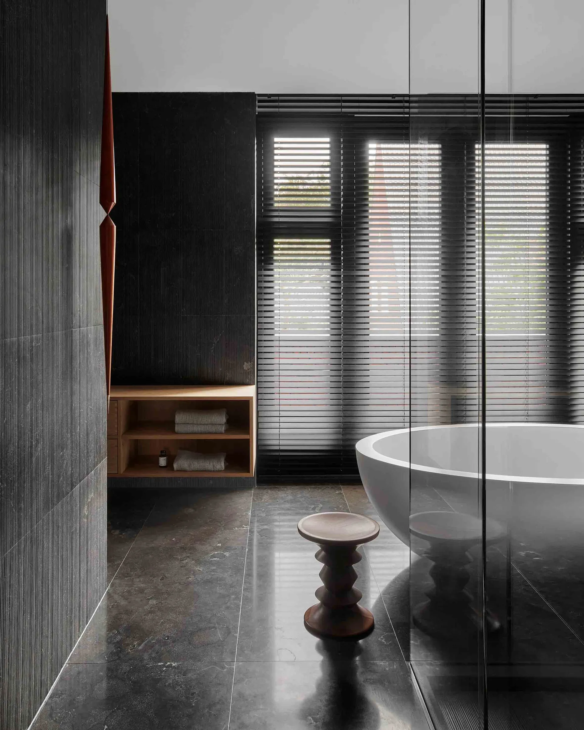A modern bathroom featuring black granite flooring and walls with a freestanding bathtub and wooden stool with a minimalistic