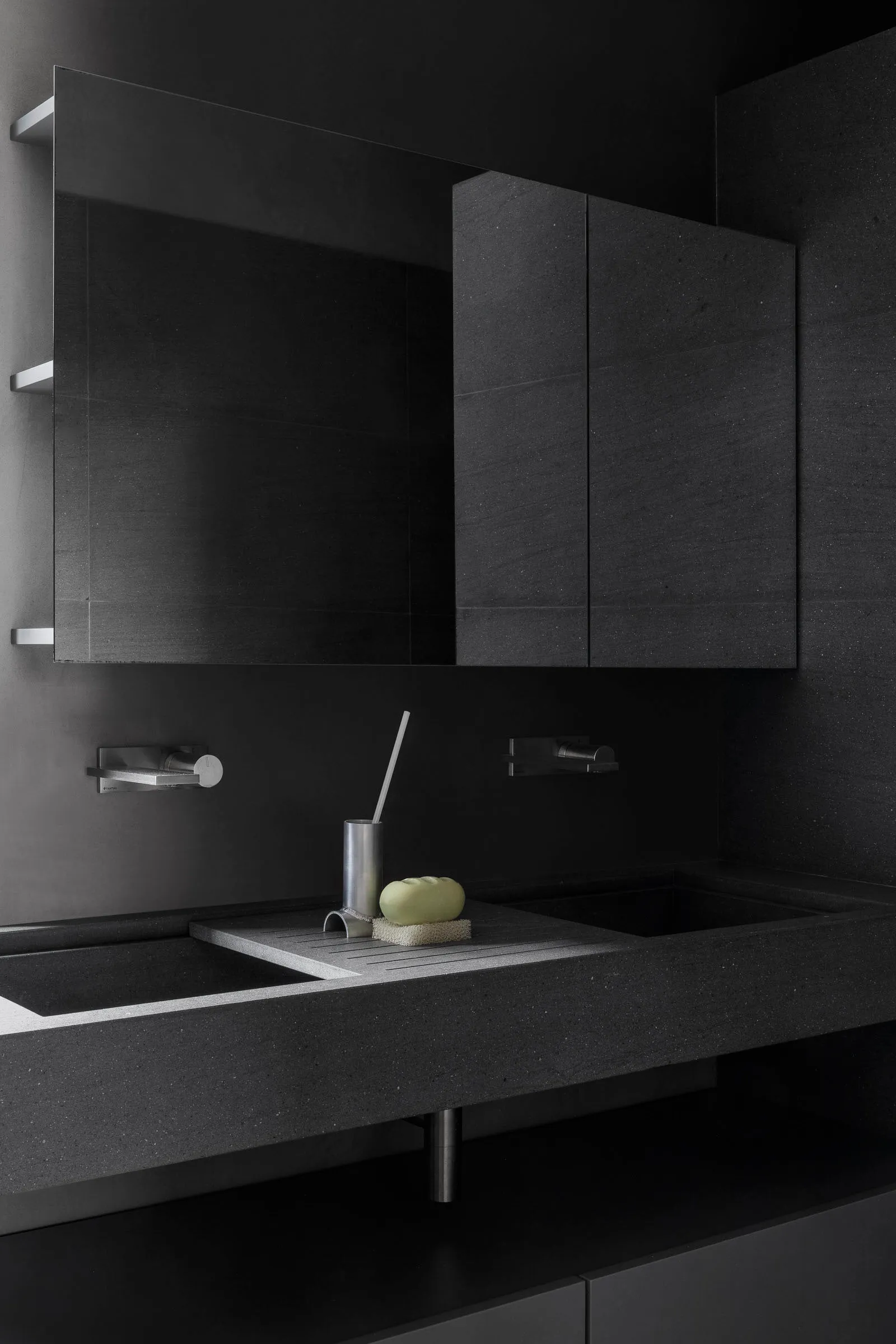A modern bathroom with a black concrete countertop and double sinks, featuring a minimalist design with sleek silver faucets
