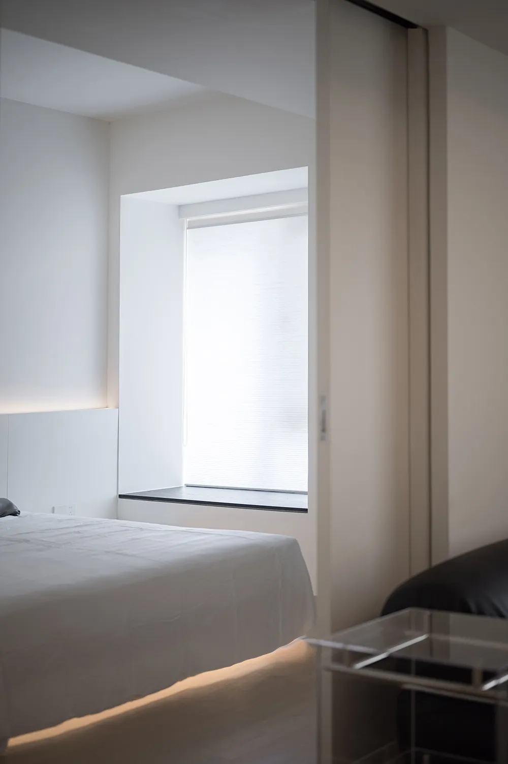 Modern minimalist bedroom with white walls, bed, and furniture.