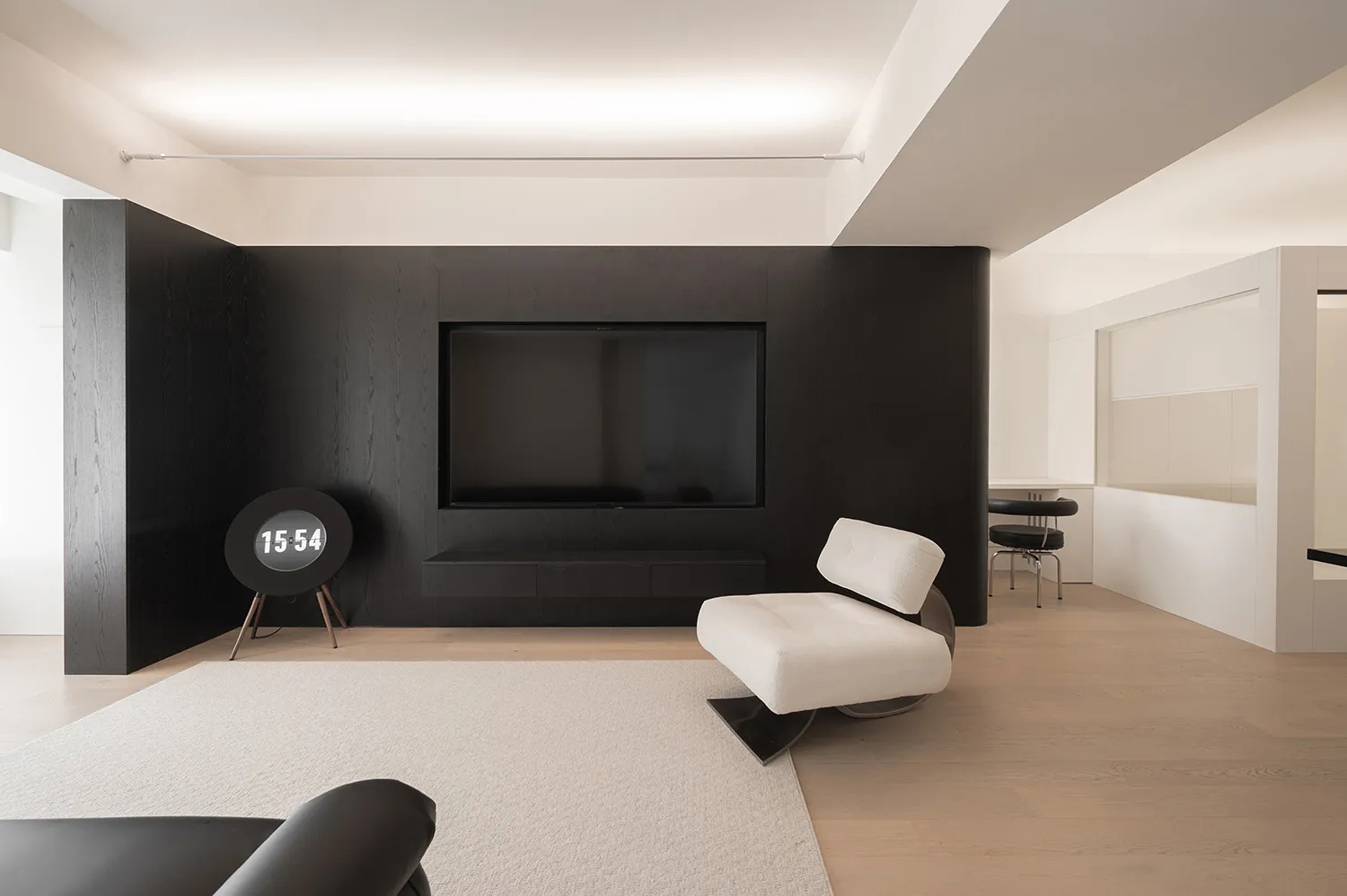 The minimalist living room features black and white decor, with a sleek black wall-mounted TV, white armchair, and wooden flo