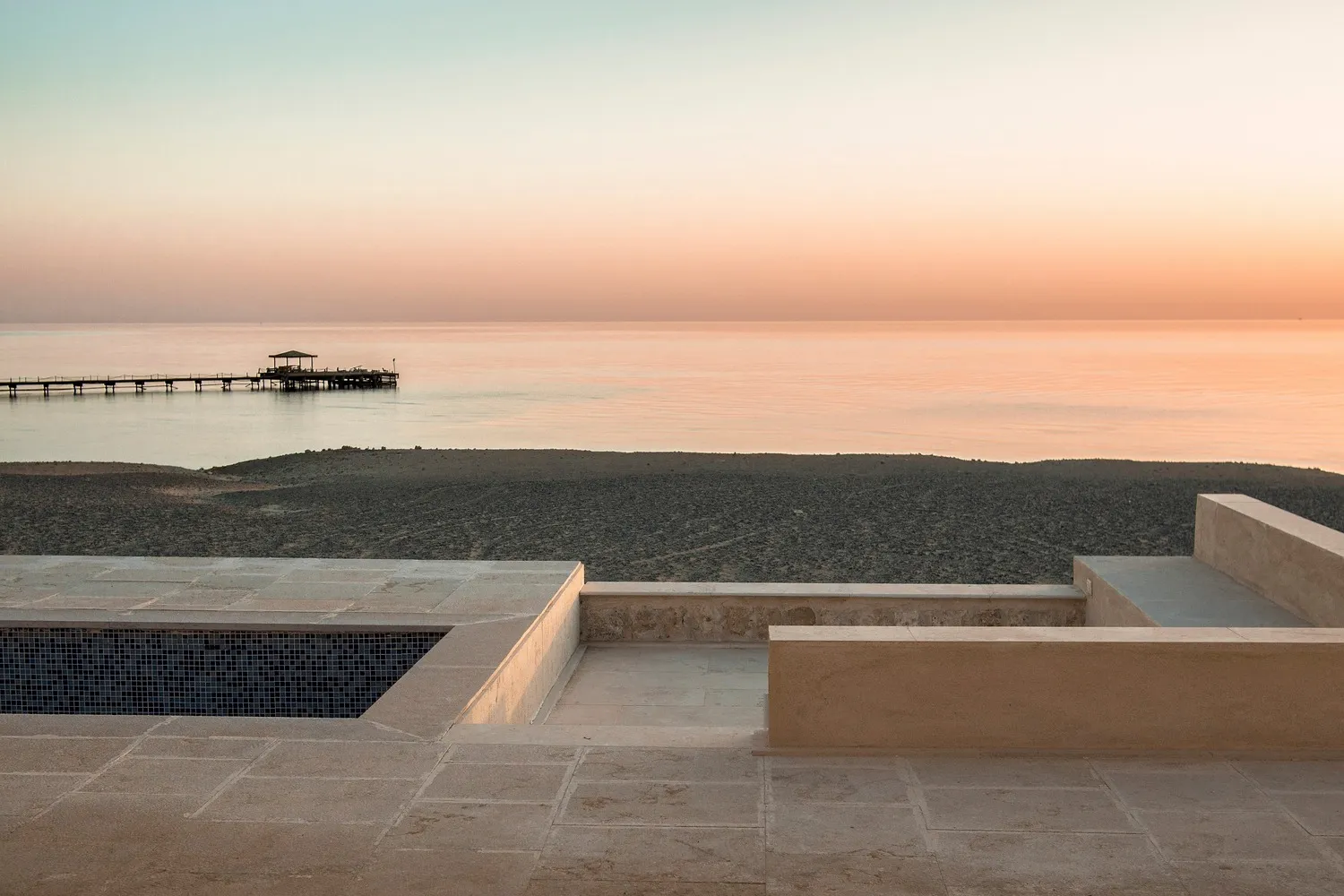 Minimalist pool deck with concrete patio and swimming pool overlooking calm ocean water.
