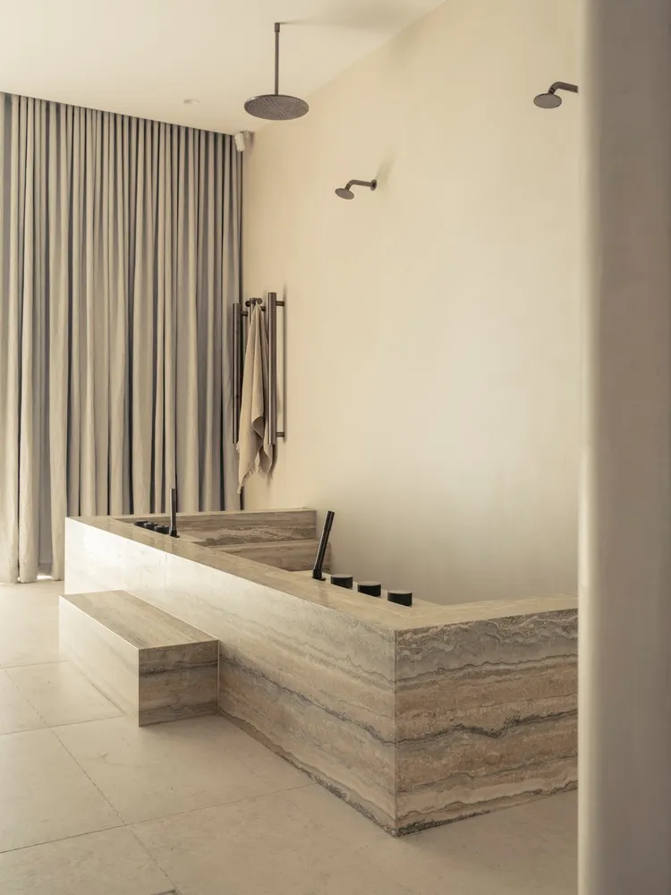 A minimalist marble bathroom with a large freestanding bathtub, modern fixtures, and a frosted glass shower door.