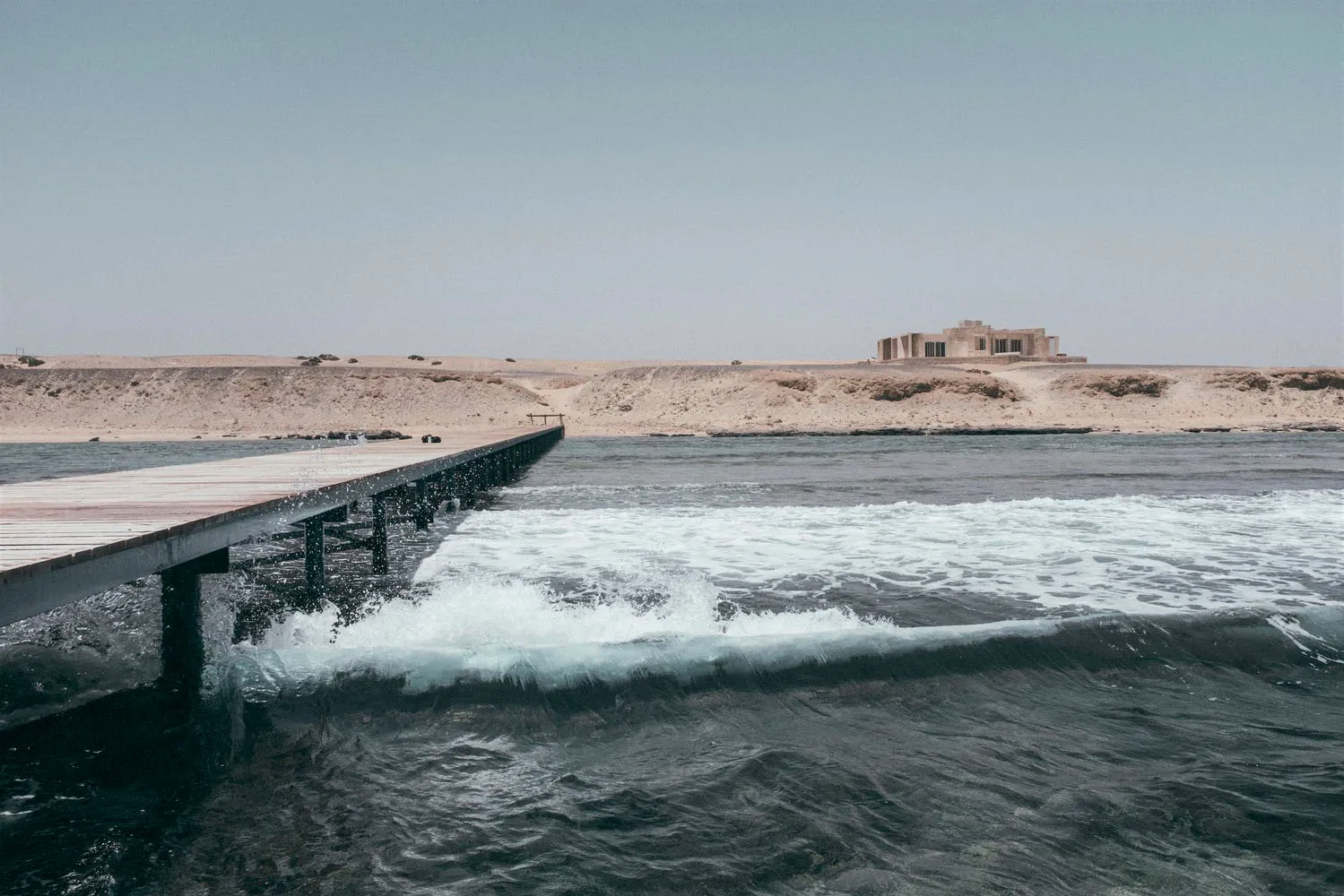 A wooden pier extending into the ocean with concrete structures in the background.