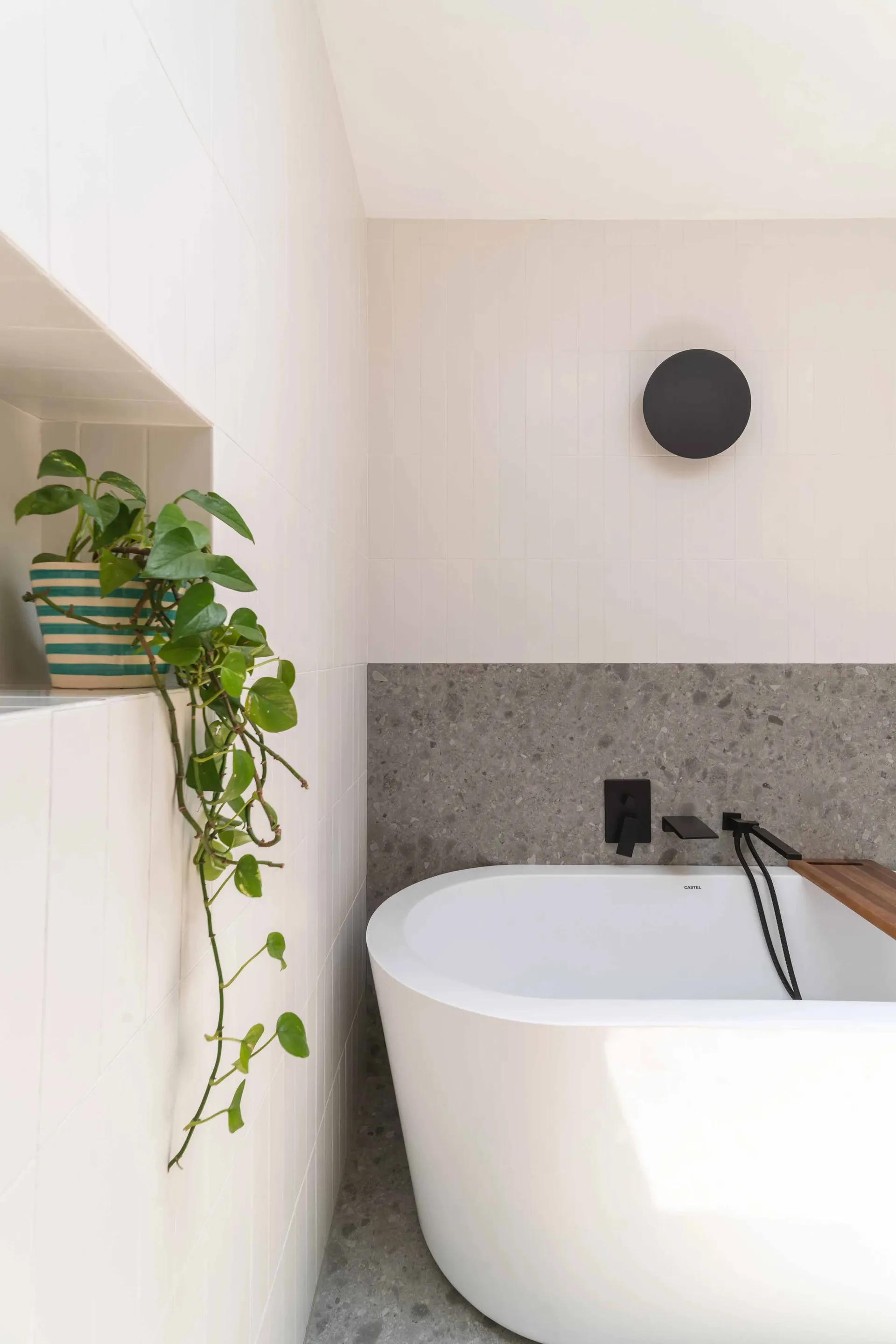 A minimalist bathroom with a white terrazzo bathtub and a green pothos plant.