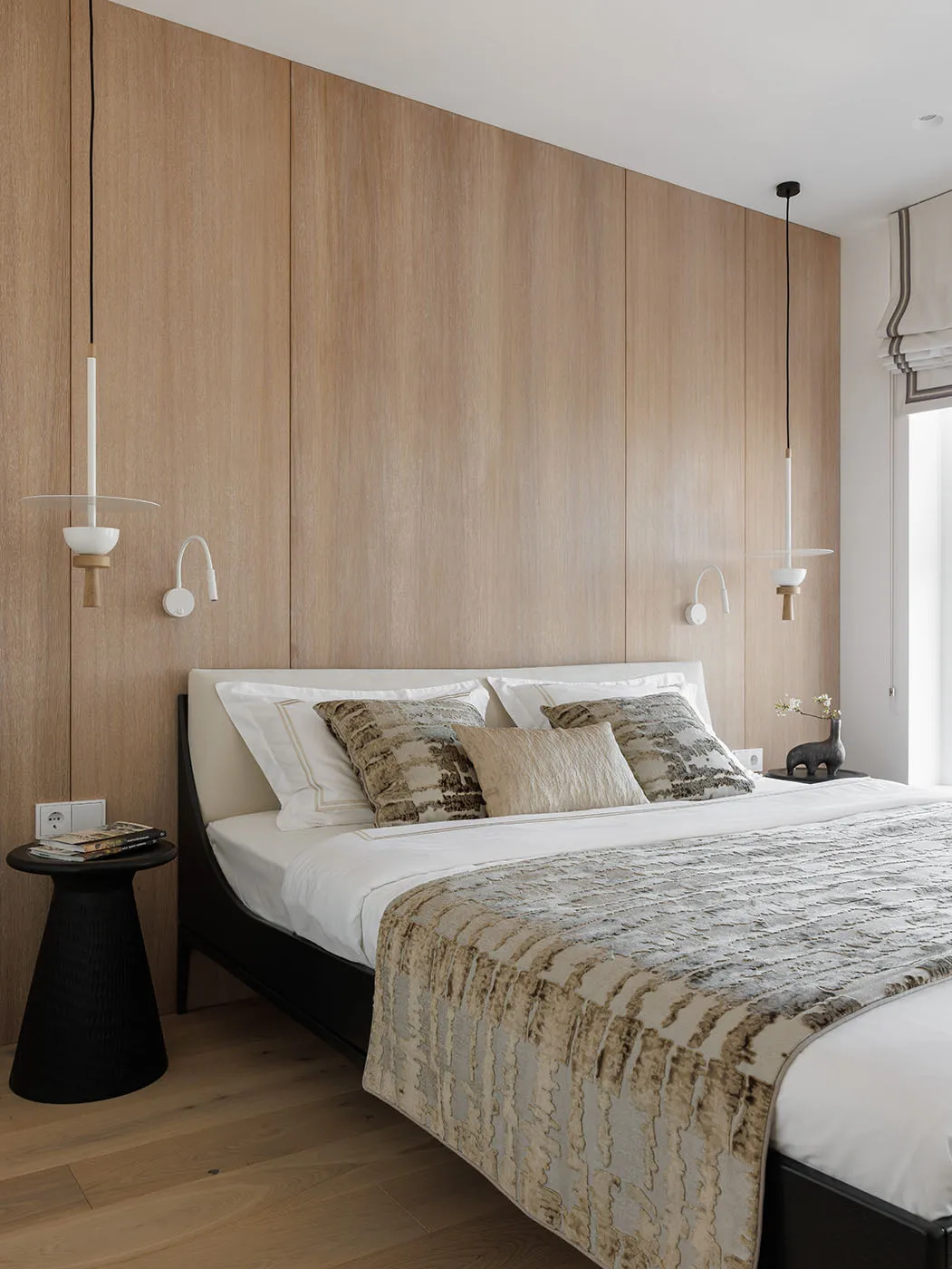 Modern minimalist bedroom with wooden walls and fabric bedding and pillows, featuring unique pendant lights and a low-profile