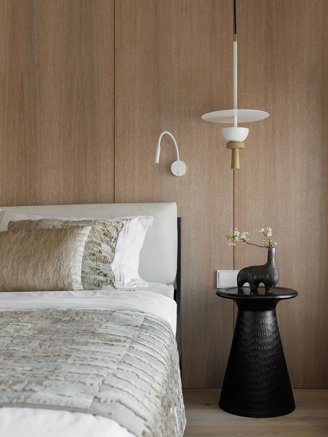 Modern minimalist bedroom featuring a bed with white bedding and pillows, a black side table with a vase and branch, and a wo