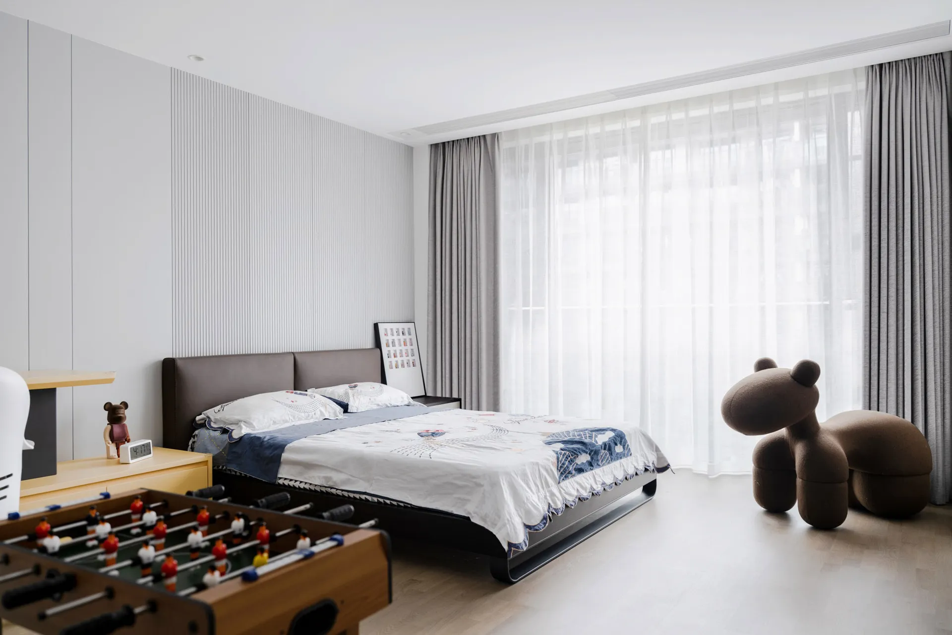 A minimalist bedroom featuring wooden furniture and a large window with sheer curtains.