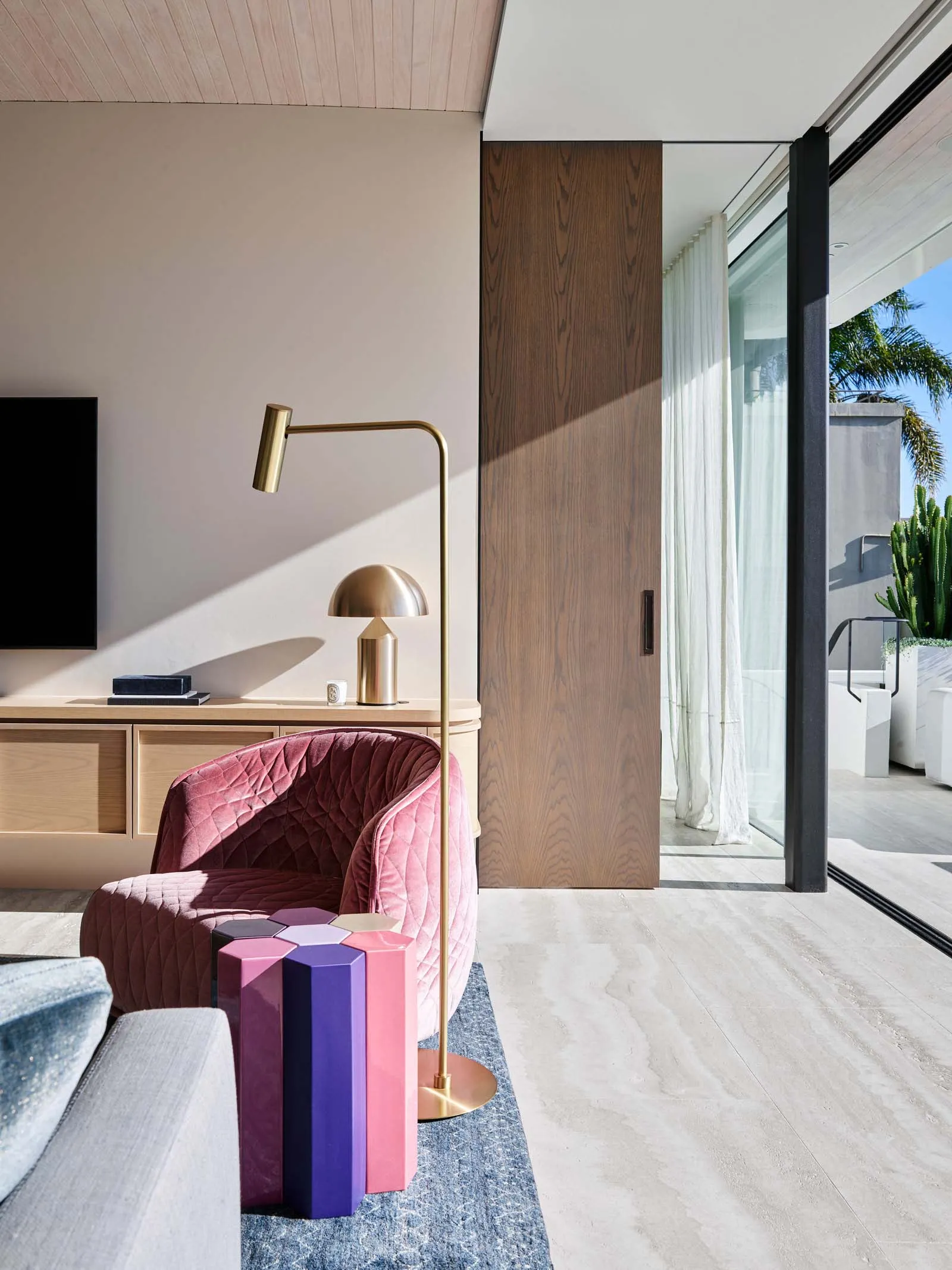 A modern living room with a pink upholstered armchair, a metallic floor lamp, and a wooden cabinet