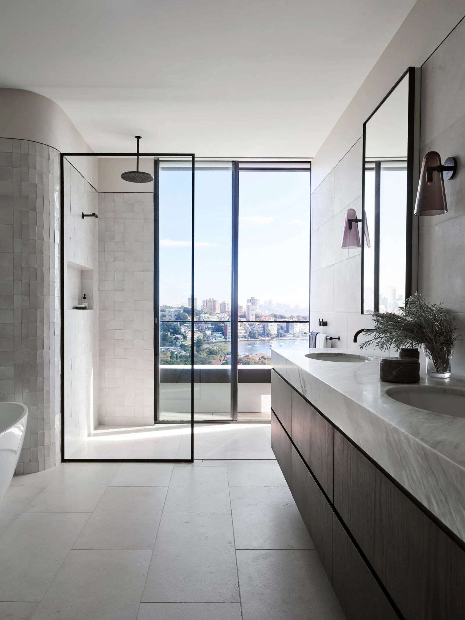 A modern minimalist bathroom featuring marble flooring, a glass-enclosed shower, and expansive windows overlooking a cityscap