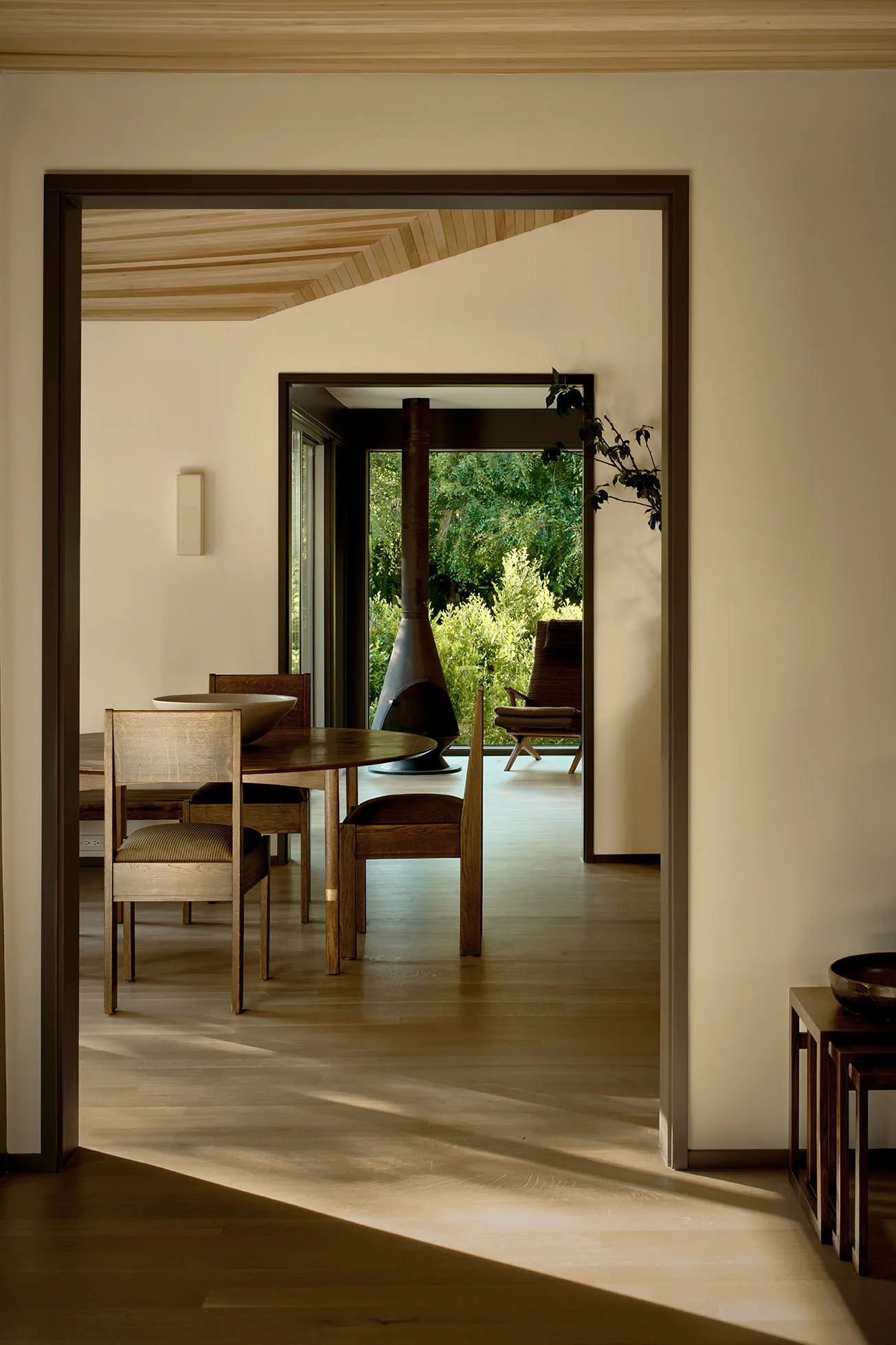Modern minimalist dining room featuring a natural wood dining table and chairs, with a view of the outdoors through large win